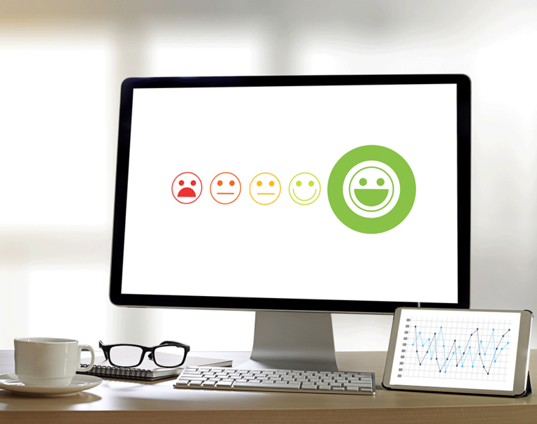 Desk with computer monitor showing a series of emoticons from angry to happy with the green happy face selected